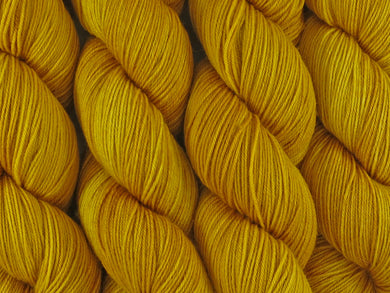 A close up of semi-solid deep golden yellow coloured skeins of superwash merino and nylon 4ply fingering sock yarn (Turmeric on Tough Stocking)