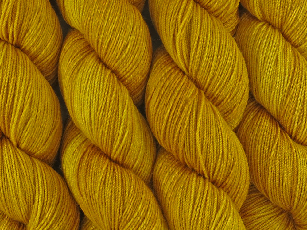 A close up of semi-solid deep golden yellow coloured skeins of superwash merino and nylon 4ply fingering sock yarn (Turmeric on Tough Stocking)