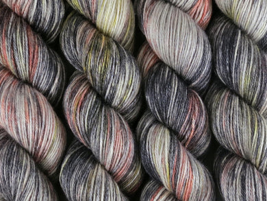 A close up of variegated black, charcoal, silver grey and white with flashes of bright to golden yellow and paprika coloured skeins of superwash merino and silk 4ply fingering sock yarn (Urban Sprawl on Silk Stocking)