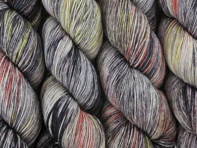 A close up of variegated black, charcoal, silver grey and white with flashes of bright to golden yellow and paprika coloured skeins of superwash merino and nylon 4ply fingering sock yarn (Urban Sprawl on Tough Stocking)