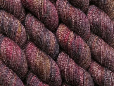 A close up of variegated warm black-brown with hints of golden yellow and rich red coloured skeins of superwash bluefaced leicester, silk and cashmere 4ply fingering sock yarn (Vegemite on Blue Chip Stocking)