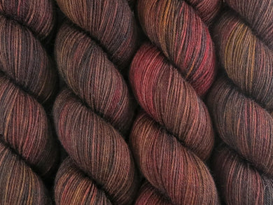 A close up of variegated warm black-brown with hints of golden yellow and rich red coloured skeins of superwash merino and nylon 4ply fingering sock yarn (Vegemite on Tough Stocking)