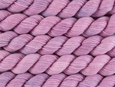 A close up of semi-solid dusty pink with hints of mauve and grey mini skeins of superwash merino and nylon 4ply fingering sock yarn arranged horizontally (Vintage Rose on Tough Stocking Mini)