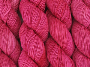 A close up of semi-solid medium pink with hints of crimson and carmine coloured skeins of superwash merino and nylon 4ply fingering sock yarn (Watermelon on Tough Stocking)