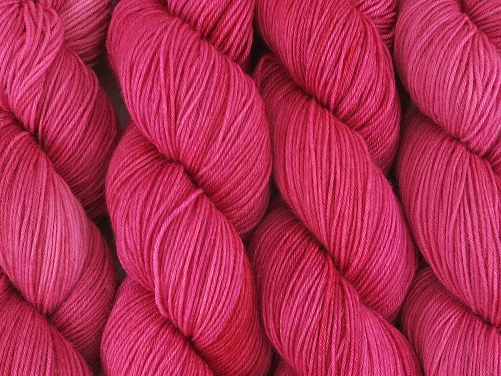 A close up of semi-solid medium pink with hints of crimson and carmine coloured skeins of superwash merino and nylon 4ply fingering sock yarn (Watermelon on Tough Stocking)