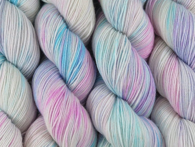 A close up of variegated white, soft pink, blue and violet coloured skeins of superwash merino and nylon 4ply fingering sock yarn (White Opal on Tough Stocking)