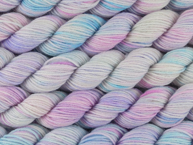 A close up of variegated white, soft pink, blue and violet mini skeins of superwash merino and nylon 4ply fingering sock yarn arranged horizontally (White Opal on Tough Stocking Mini)